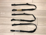 Three black TOIM customizable quick adjust two point slings with custom text engraved on the pull tabs lying on the floor.